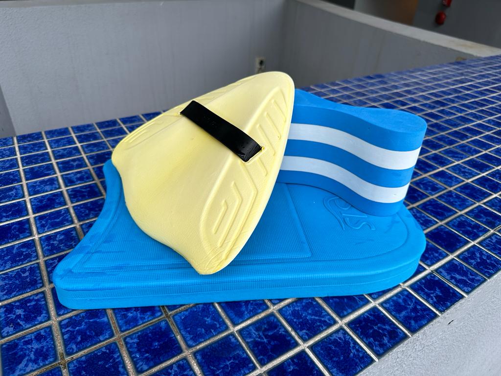 A collection of swimming training aids including an alignment board, kick board, and pull buoy arranged beside a swimming pool, fundamental tools for improving swimming skills in swim lessons.