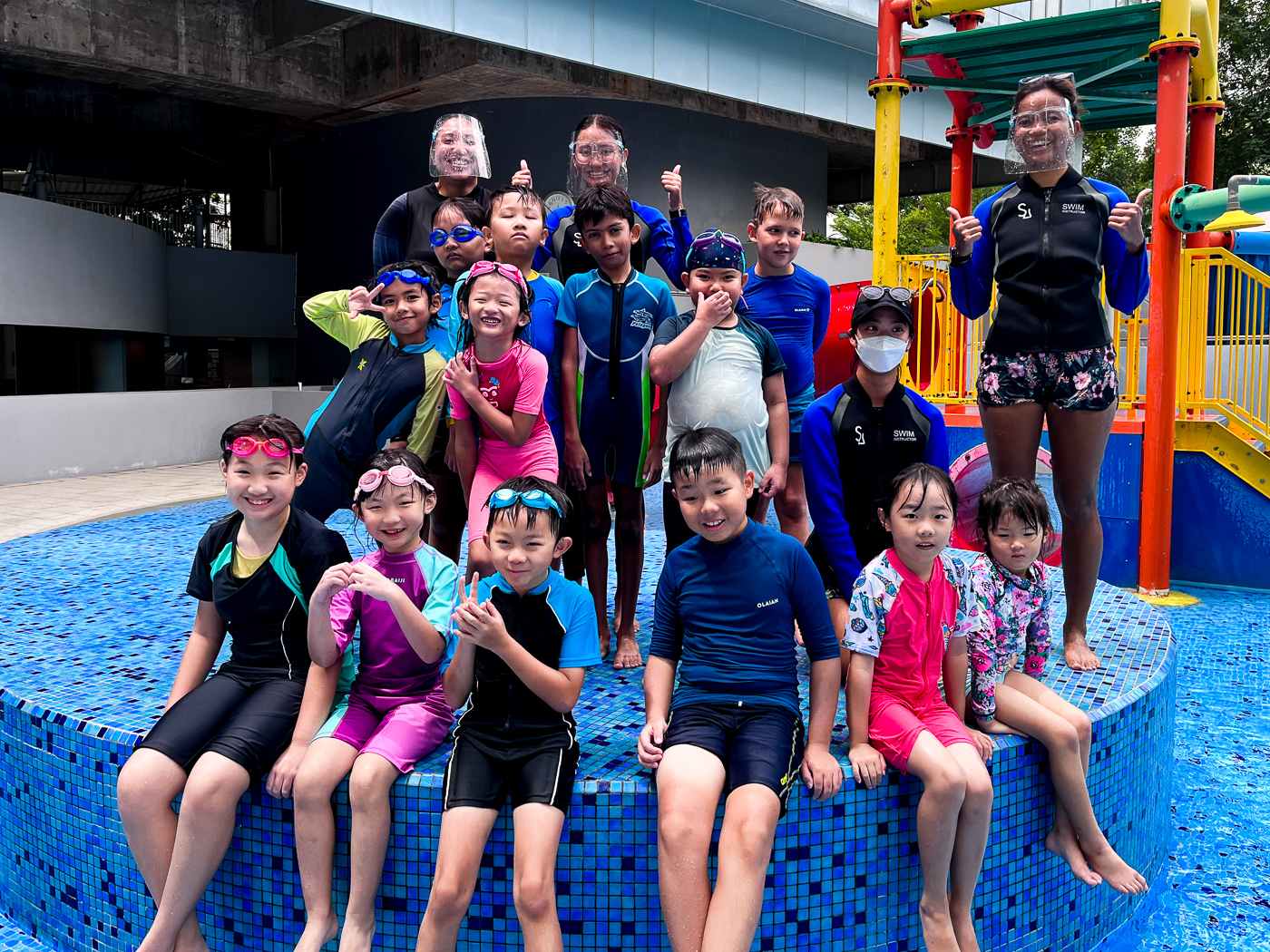 Group of joyful kids posing in front of the water playground equipment at the NTU@one-north swimming pool.