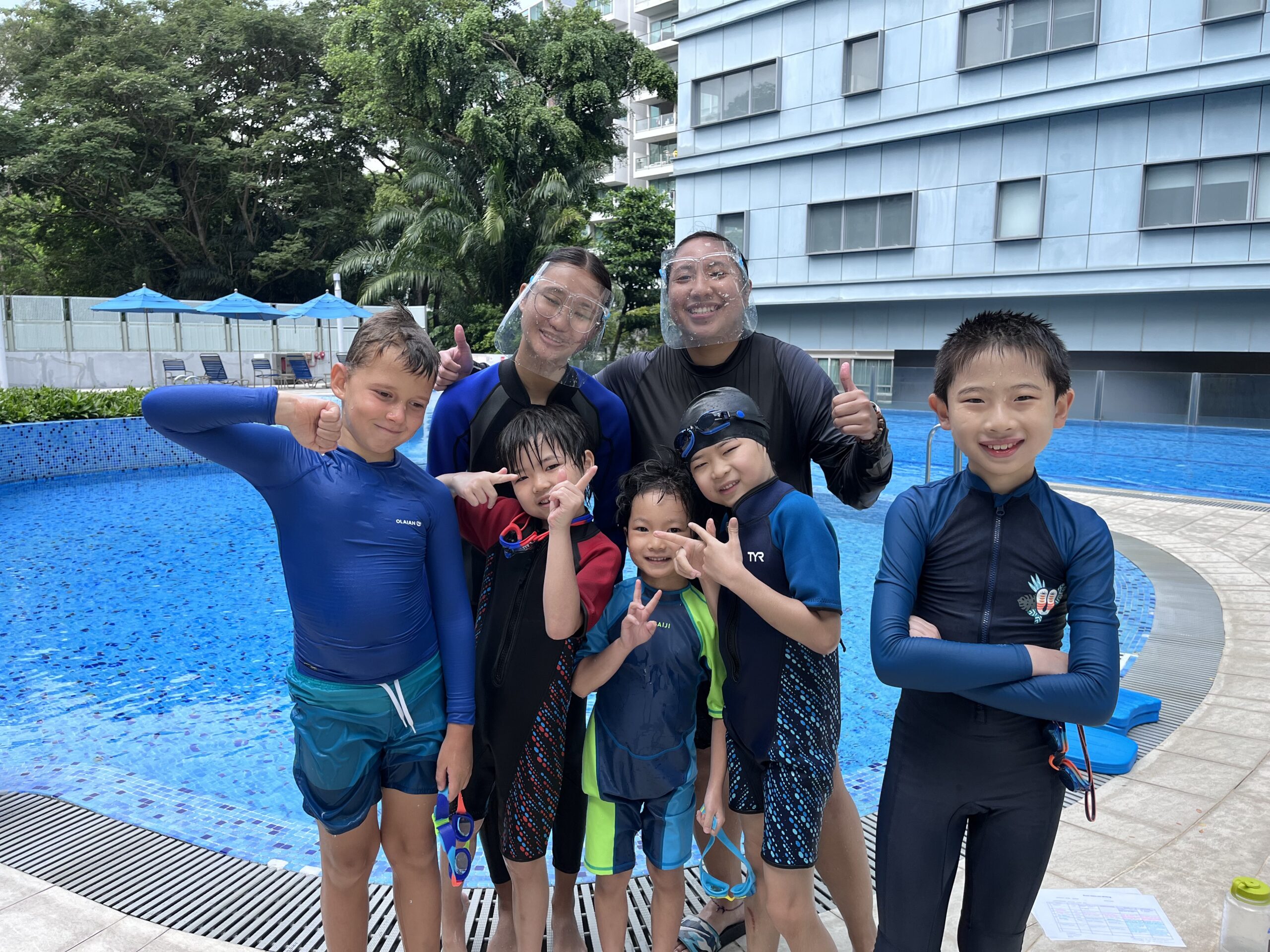 Group of smiling kids standing next to Swim Lab's sparkling swimming pool, ready for their swim lesson.