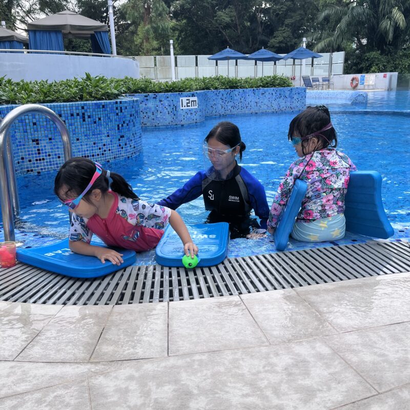 Coach guiding two children during a swimming lesson in a pool.
