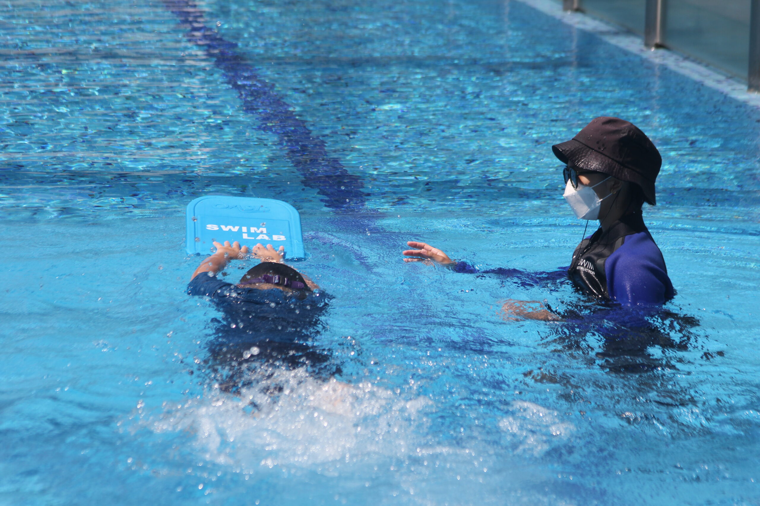 Swim coach guiding a young child in a swimming pool during a lesson.