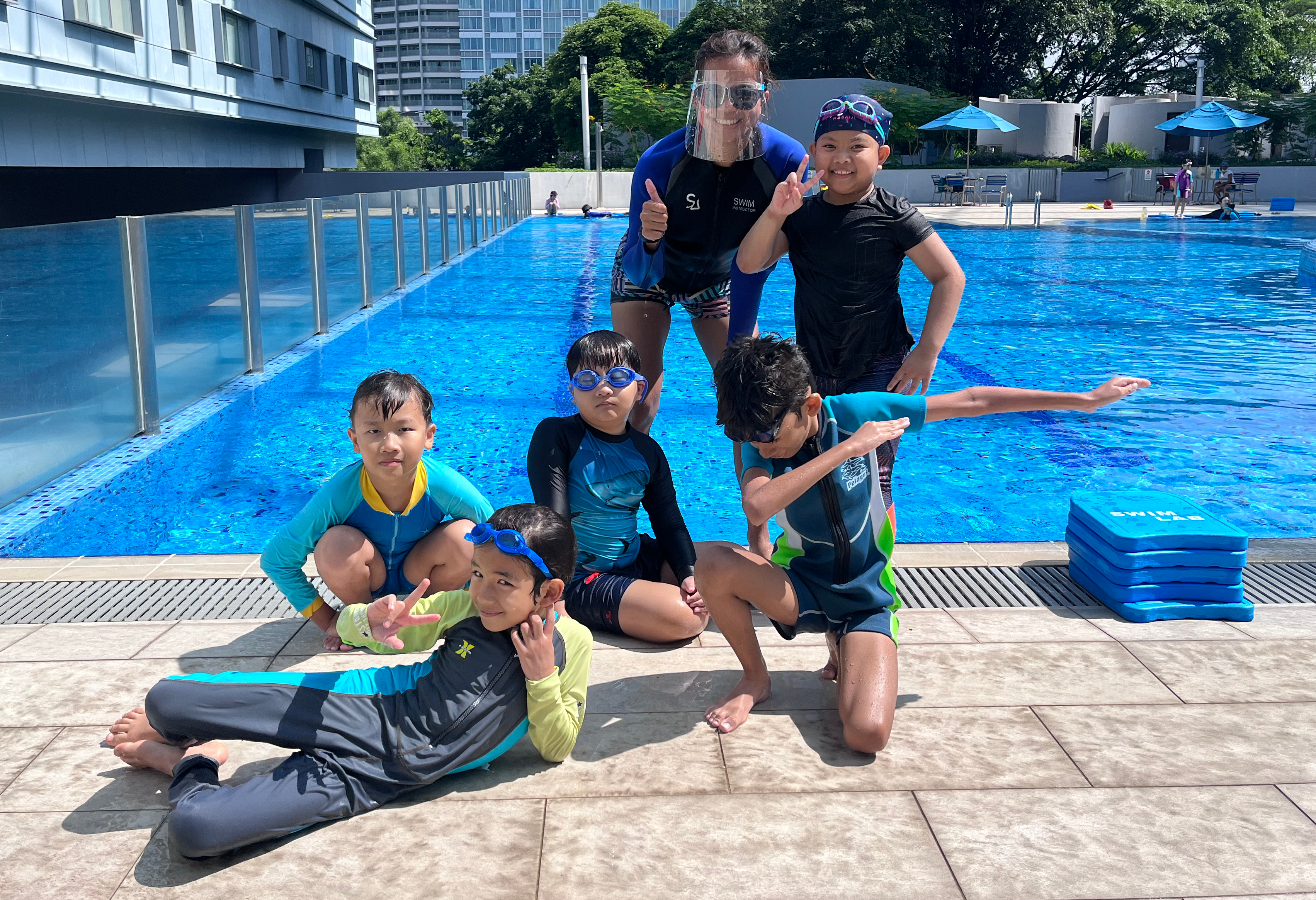 Group of children smiling in front of Swim Lab pool, representing different age groups and swimming levels.