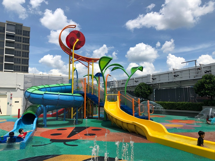 Aquatic-themed water play area in Yishun's Northpoint City featuring water slides and a dunking machine, surrounded by various food and beverage options.