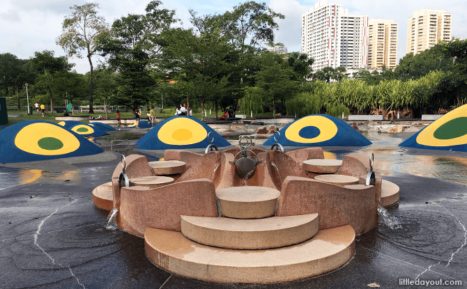 Interactive water play area with educational sluice gates, a castle for splashing, and an eco-conscious phytoremediation system, set in a secluded park location.